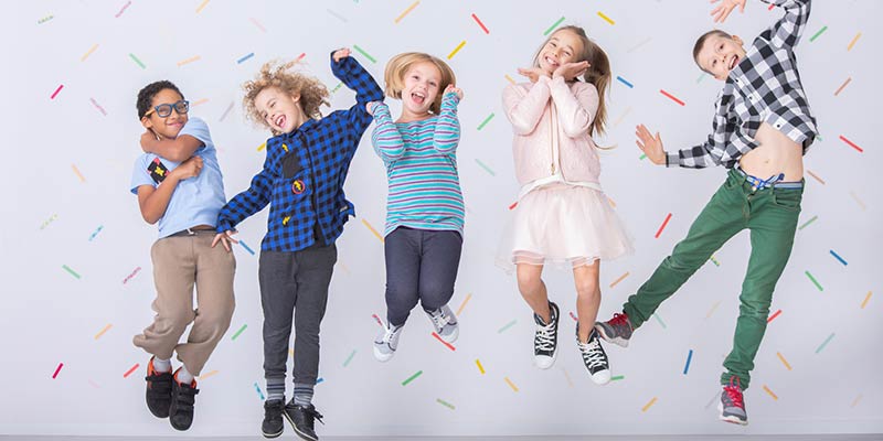 Eine fröhliche Gruppe von Kindern springt vor einer bunten Wand in die Luft